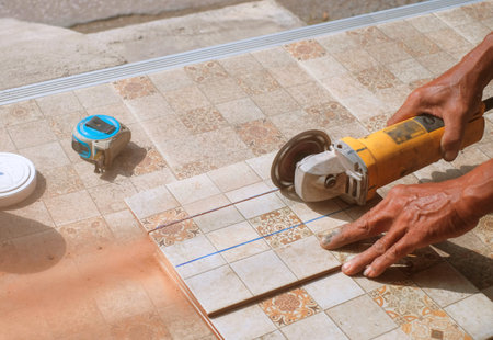 Closeup hands of laborer holding electric angle grinder working cutting aluminum lumber at construction site with sun flare background.の写真素材