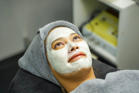 Closeup beauty woman with white mask cream on her face in beauty clinic.