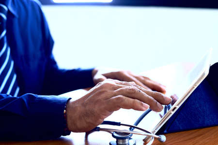 Doctor working with stethoscope and digital tablet computer in medical workspace.