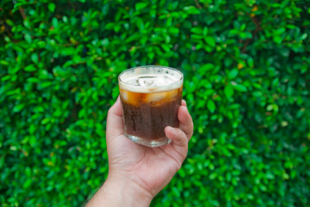Man hand holding iced coffee on green grass background, top view
