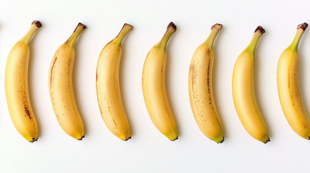 A collection of fresh bananas arranged in a linear fashion on a clean white background. The vibrant yellow color and natural texture highlight the freshness, making this image perfect for health and wellness themes.の素材