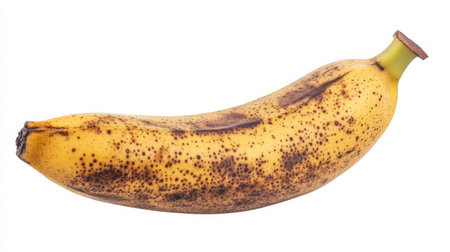 A ripe banana with brown spots sits on a white background, showcasing its natural texture and vibrant color. Ideal for health, food, and nutrition themes.の素材