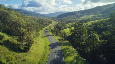 Explore a breathtaking aerial view of a winding road nestled between lush green hills under a bright sky. Perfect for travel and nature themes.の素材