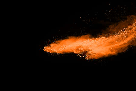 Freeze motion of Orange powder exploding, isolated on black background. Abstract design of red dust...