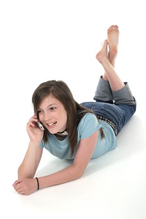 Cute young teenage girl sitting on the floor and talking on a cellphone; shot on whiteの写真素材