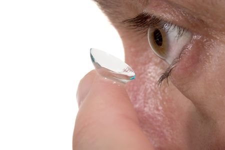 Closeup view of a man's brown eye while inserting a corrective contact lens on a finger with a white background.の写真素材
