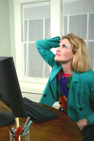 Beautiful middle aged executive business woman with her hand on her head thinking at a computer in the office.の写真素材