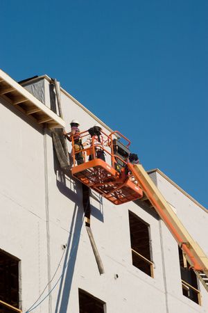 Two construction workers on a cherry picker working on a building under construction. Worker faces are hidden and not recognizable in the image.の写真素材