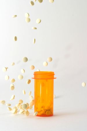 medicine bottle on table with white tablets falling into and around it; bottle is placed in the center of the frame with pills frozen in stop motion falling into and around the bottleの写真素材