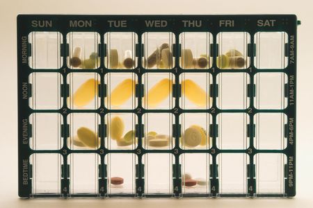Organizer for medications with compartments for keeping track of daily doses of medicine over a week timespan; Organizer is upright, centered, fills the frame, and is lighted from behind making some pills appear translucentの写真素材