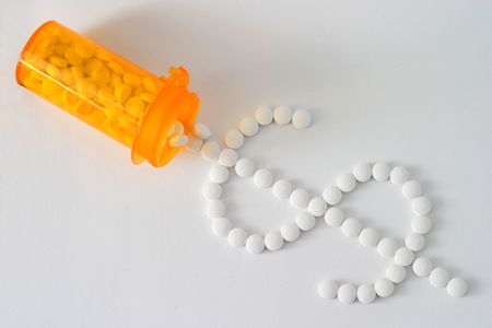 medicine spilling onto white table from orange bottle into a dollar sign shape; medicine is white pills forming a diagonal across the frameの写真素材