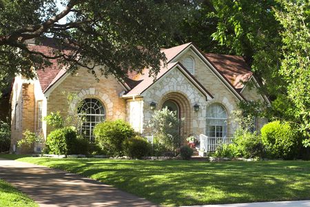 house with beautiful mixture of light colored and white stone and brick; arched windows and entryway; surrounded by green foliageの写真素材