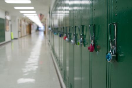 Closeup view of a lock on a school locker with row of lockers and and empty school hallway in background out of focus from depth of field.の写真素材