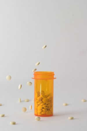 medicine bottle on table with white tablets falling into and around it; bottle is placed in the center of the frame with pills frozen in stop motion falling into and around the bottleの写真素材