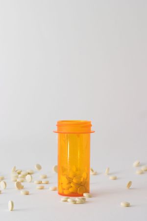 medicine bottle on table with tablets around it; bottle is placed in the center of the frame with some pills in the bottle and some laying around itの写真素材