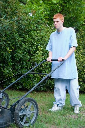 Red-haired teenaged young man mowing the lawn on a bright summer day.の写真素材