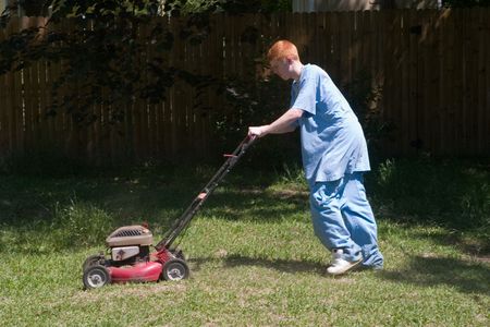 Red-haired teenaged young man mowing the lawn on a bright summer day.の写真素材
