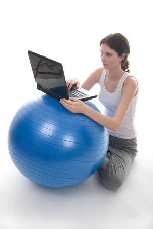 Young woman in casual clothes sitting on the floor with a laptop computer on top of an blue exercise ball used as a make-shift desk.の写真素材