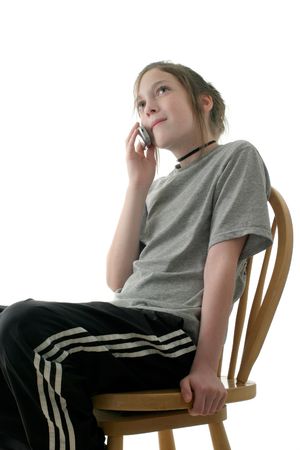 young teen girl sitting on chair and talking on cellphone; isolated on white backgroundの写真素材