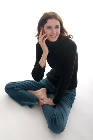 Casual young brunette woman sitting cross-legged on the floor, smiling, and talking on cell phone.の写真素材