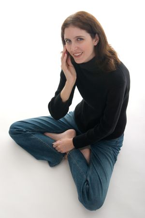 Casual young brunette woman sitting cross-legged on the floor, smiling, looking directly at camera, and talking on cell phone.の写真素材