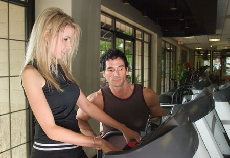 Man and woman exercising together at a fitness center on a treadmill walker exercise machine.  Man could be a personal fitness trainer.の写真素材