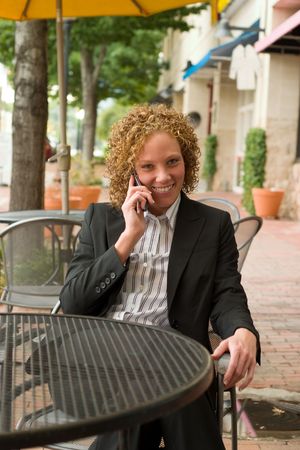 Smiling business woman relaxing on the sidewalk while discussing business on a cellphone.の写真素材