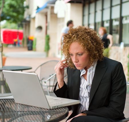 Young business woman deep in thought sitting in a chair on a city sidewalk looking at a laptop computer screen.の写真素材