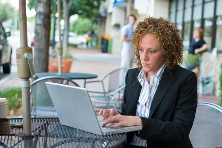 Young business woman deep in thought sitting in a chair on a city sidewalk looking at a laptop computer screen.の写真素材