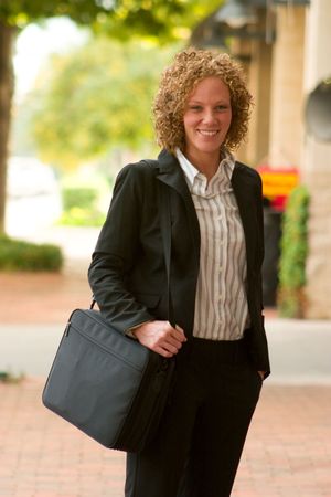 Smiling business woman carrying a briefcase strolling down a city sidewalk.の写真素材