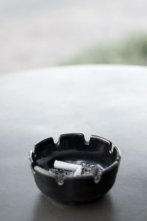 An ashtray with cigarette butts and ashes on a table.  Limited depth of field with focus on ashes.の写真素材