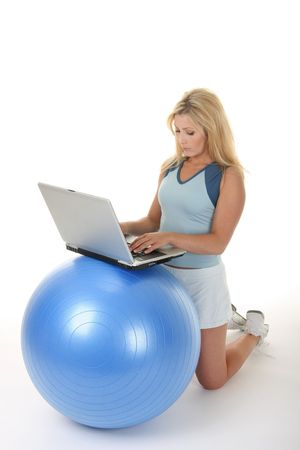Attractive young blonde woman using an exercise ball as a desk for her laptop computer.の写真素材