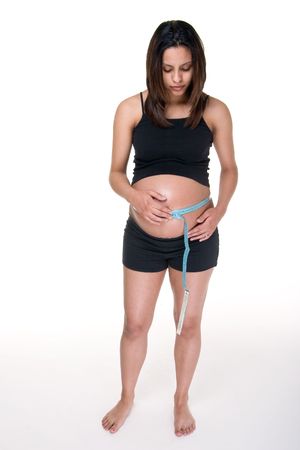 Young pregnant Hispanic woman using measuring tape to measure her abdomen to find out how much her unborn  has grown.の写真素材