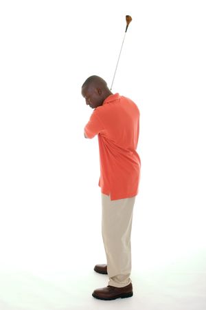Casual young African American man in a bright orange golf shirt swinging a golf club.の写真素材
