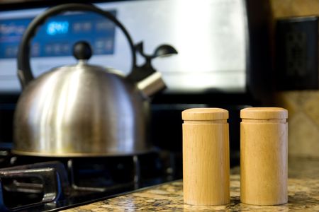Close up of salt and pepper shakers with kettle and oven in background