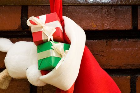 Gift boxes with ribbon in a Christmas sock hanging on fireplace mantel