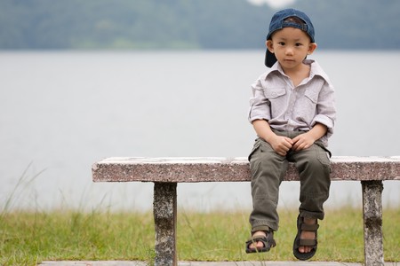 Asian little boy sits on a bench in a parkの写真素材