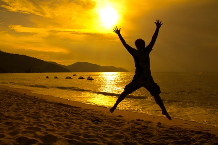 Silhouette happy man jumping on the beach during sunsetの写真素材