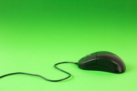 Black computer mouse on green background with cord showingの写真素材