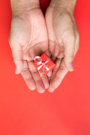 Red gift box with ribbon in hand isolated in red backgroundの写真素材