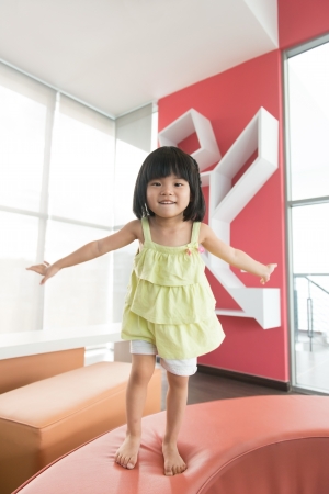 Little Asian girl jumping on sofa happilyの写真素材