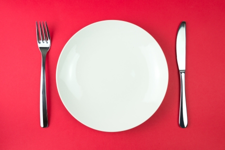An arrangement of a white dinner plate with fork and knife, isolated on a red backgroundの写真素材