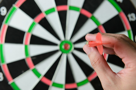 Hand aims a dart as ready to throw it at the target