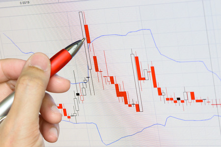 Close up of hand holding pen pointing graph chart on monitorの写真素材