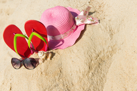 Red flip flop with sunglasses and pink floppy hat on beachの写真素材
