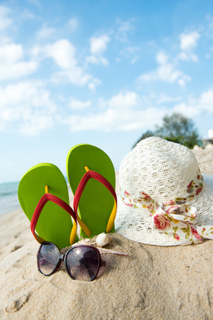 Green flip flop, sunglasses and floppy hat at the beachの写真素材