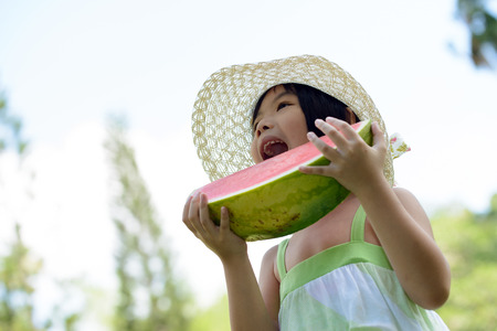 Asian kid have a big bite on watermelon in parkの写真素材
