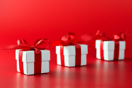 Three white gift boxes with ribbons on red background