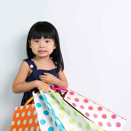 Little Asian girl holding shopping bags on white backgroundの写真素材