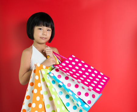 Little Asian girl holding shopping bags on red backgroundの写真素材
